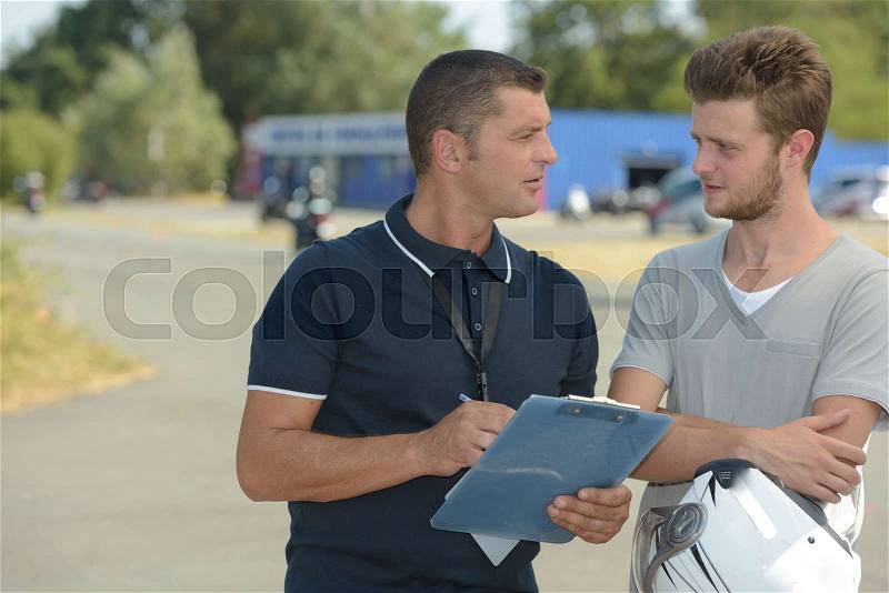 Happy student driver with instructor filling forms before driving test, stock photo