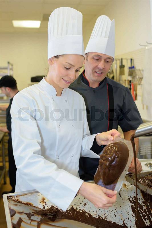 Commis chef prepares chocolate with chef checking, stock photo
