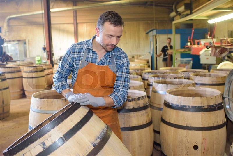 Wood barrels production cooper using hammer and tools in workshop, stock photo