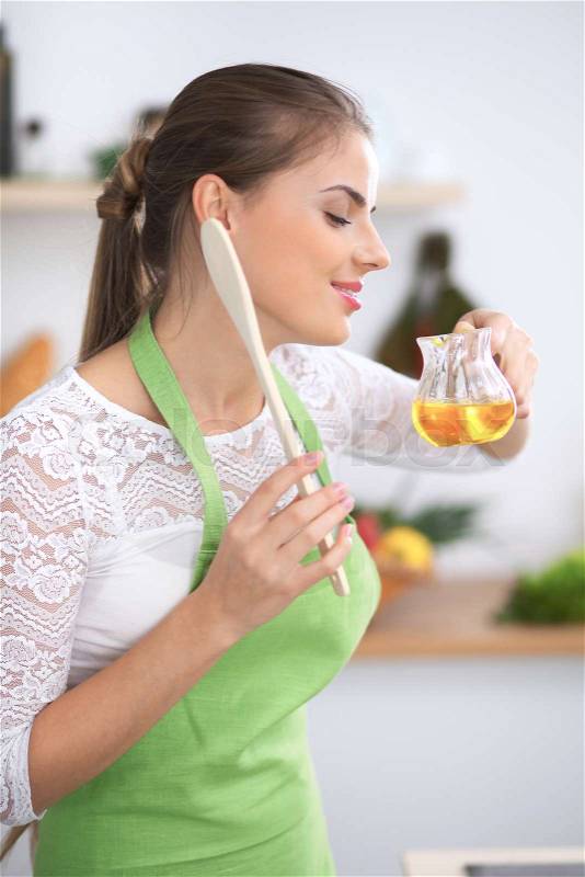 Young woman smelling the vegetable oil while enjoys cooking in the kitchen, stock photo