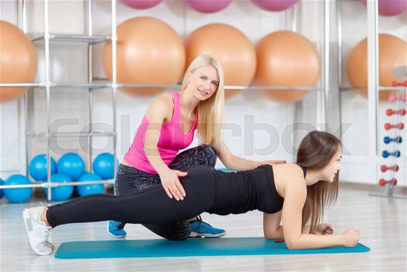 Attractive mature woman professional fitness instructor smiling to the camera while working with her client at the gym. Professional fitness trainer helping young woman at the gym, stock photo