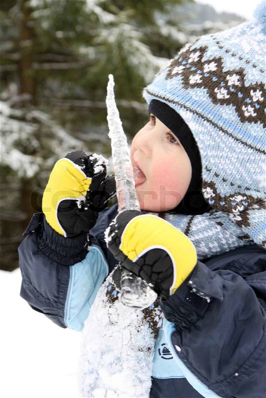 Small boy eat icicle in winter on mountains, stock photo