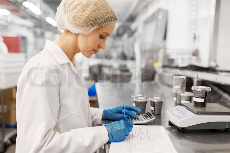 Food production, industry and people concept - woman weighing ice cream on scale and filling papers at factory, stock photo