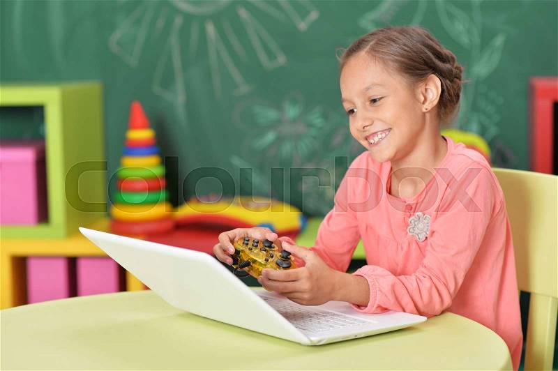 Cute little girl playing computer game on laptop with joystick, stock photo
