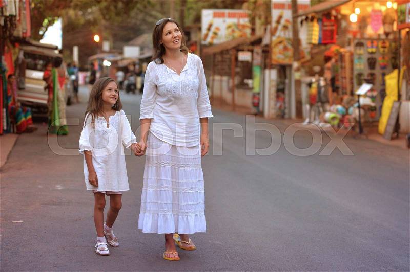 Mother and daughter wearing white clothing walking on road, stock photo