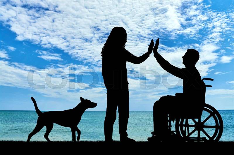A man disabled in a wheelchair with having fun with friend and dog by the sea. The concept of support and assistance to people with disabilities, stock photo