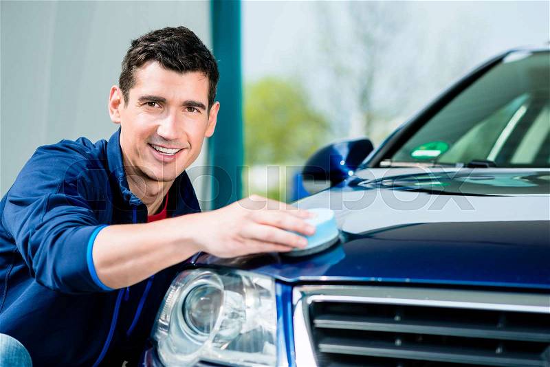 Young man using an absorbent soft towel for drying and polishing the surface of a clean blue car, stock photo