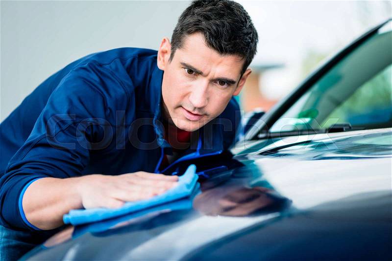 Young man using an absorbent soft towel for drying and polishing the surface of a clean blue car, stock photo