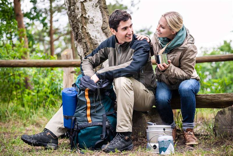 Man and woman take break from hiking and prepare food on camping stove, stock photo