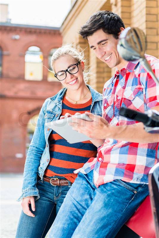 Young Couple, woman and man, on city trip in Berlin planning their Vespa tour using tablet PC, stock photo