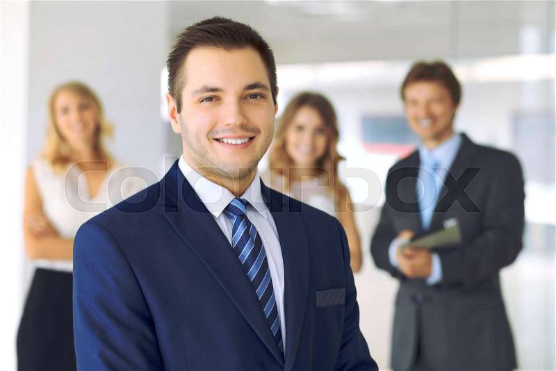 Smiling businessman in office with colleagues in the background, stock photo