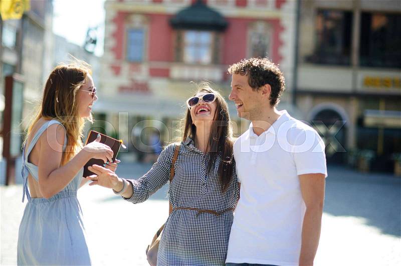 Three young people stand on the square of the ancient city. They are looking at beautiful buildings with pleasure. Friends are hugging each other. Everyone is in a good mood, stock photo
