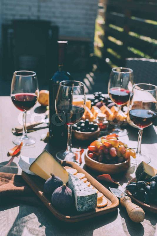 Glasses of red wine with various snacks on wooden table outdoors, stock photo