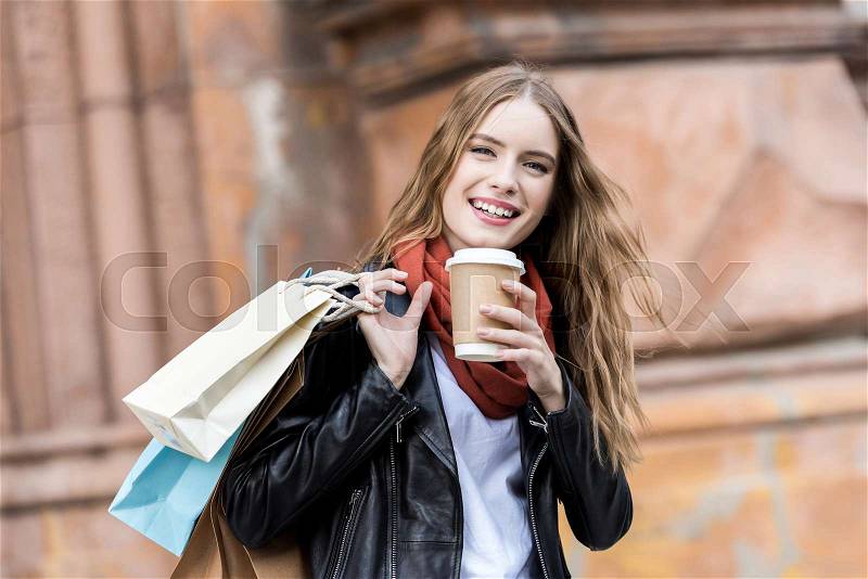 Portrait of laughing woman with shopping bags and coffee to go on street, stock photo