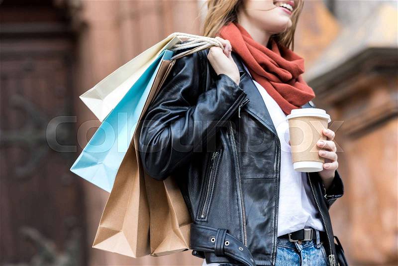 Partial view of woman with shopping bags and coffee to go on street, stock photo