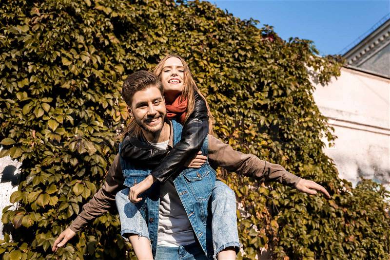 Portrait of happy couple in love piggybacking in autumn park, stock photo
