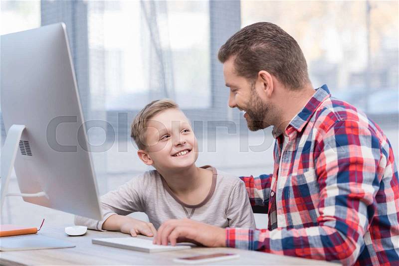 Happy father and son using desktop computer and smiling each other, stock photo