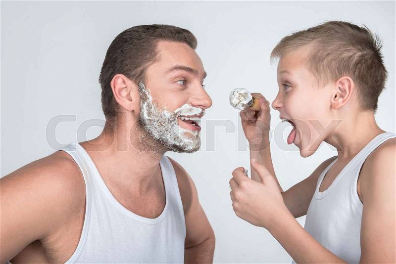 Father and son having fun while shaving together isolated on grey, stock photo