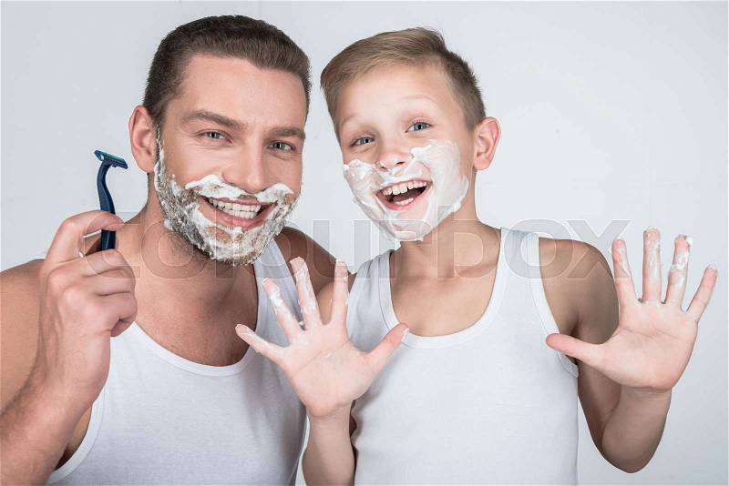 Happy father and little son with shaving foam on faces smiling at camera isolated on grey, stock photo