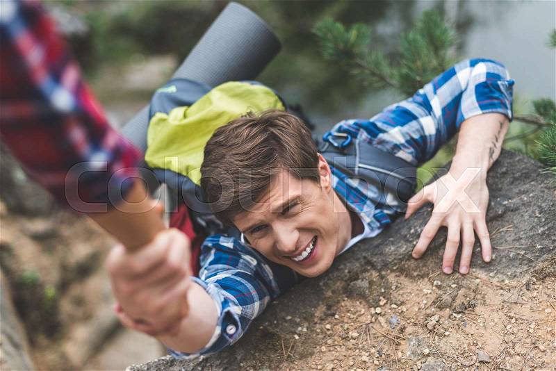 Close-up shot of woman helping exhausted boyfriend to climb rock, stock photo