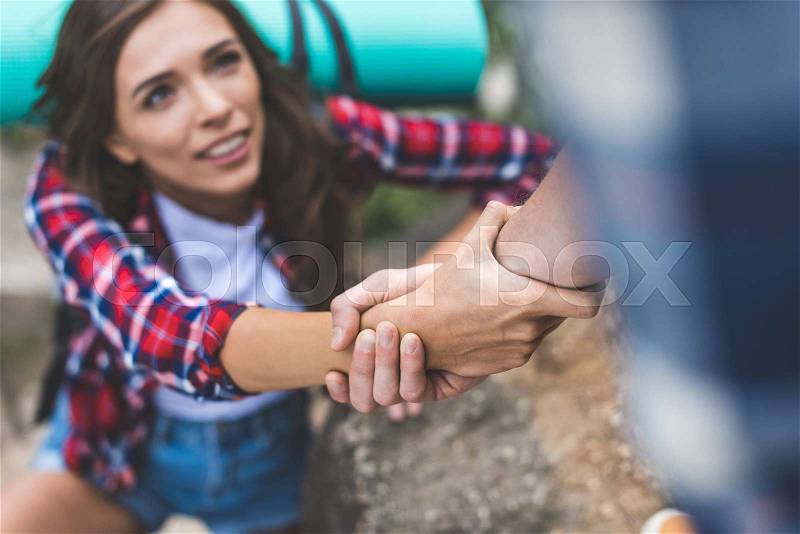 Close-up shot of man helping beautiful girlfriend to climb rock, stock photo