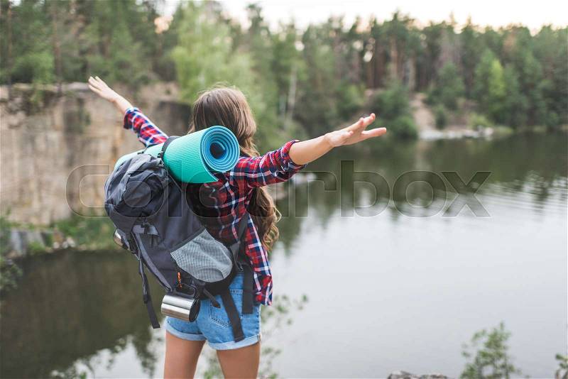 Young woman with backpack celebrating freedom on nature while looking at lake, stock photo