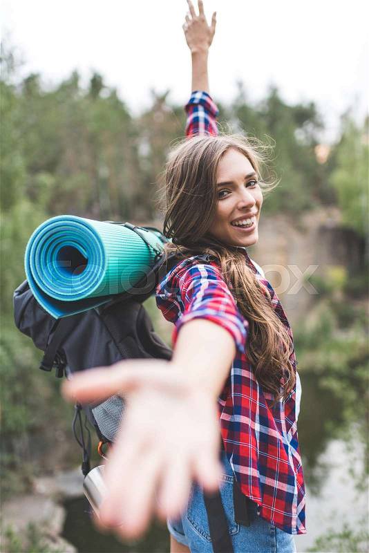 Beautiful young woman with trekking backpack stretching hand out to camera outdoors, stock photo