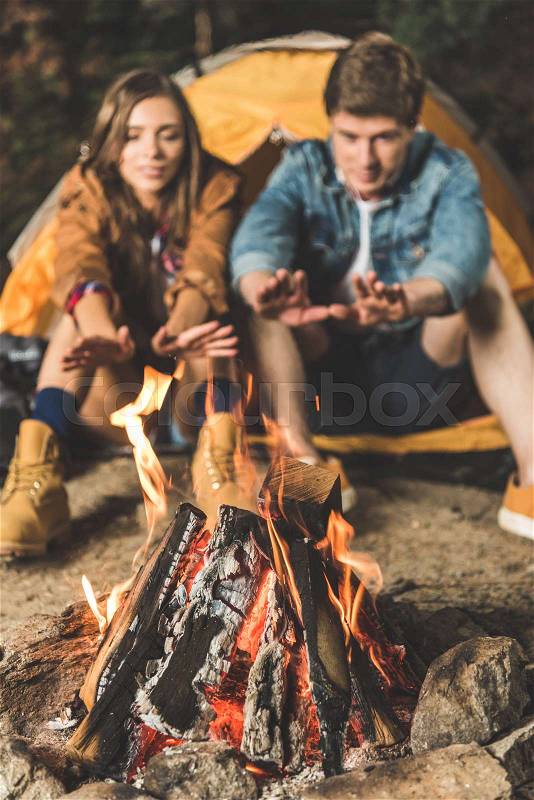 Couple warming hands with bonfire on hiking trip, stock photo