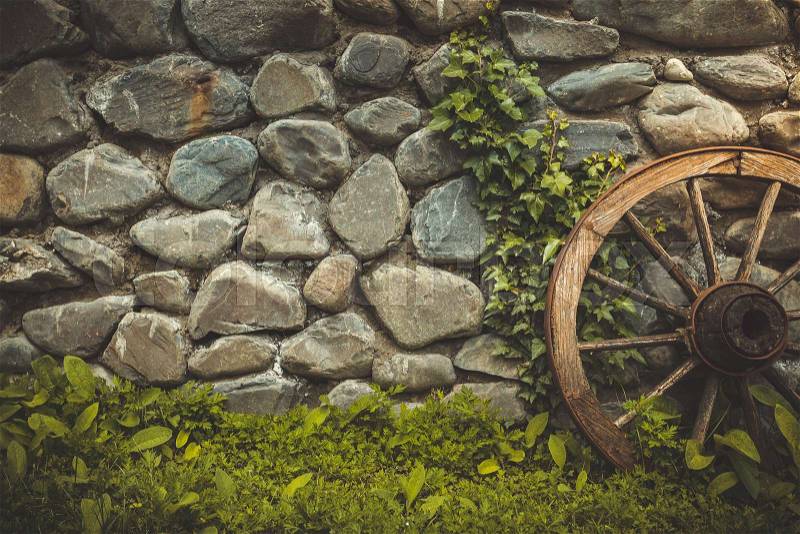 Stone wall texture background. The pattern of old stone wall with ancient wheel and green grass growing. Retro vintage toning filter, stock photo