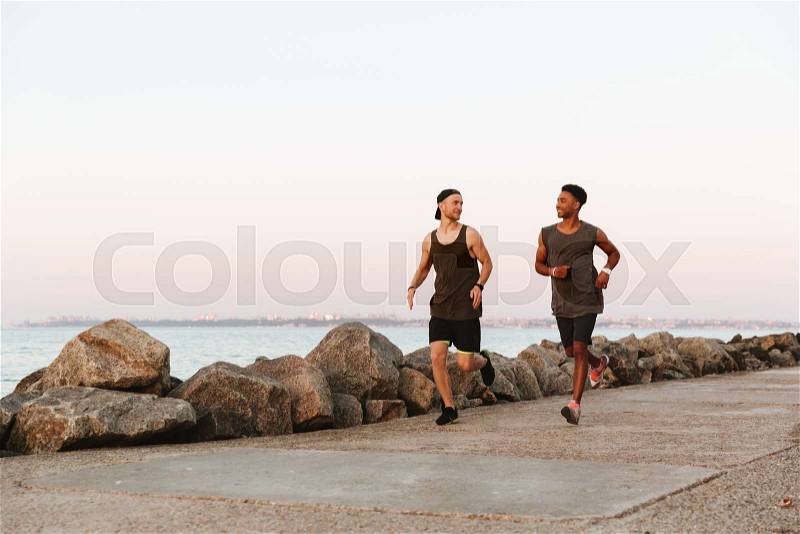 Two smiling fitness men running outdoors at the beach, stock photo