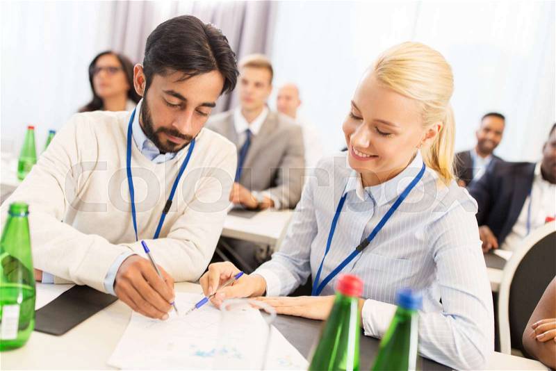 Business, people and education concept - businessman and businesswoman at international conference discussing papers, stock photo
