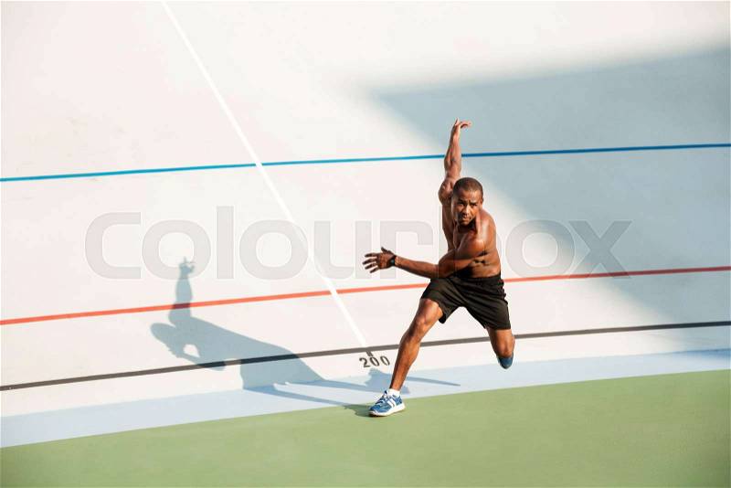 Full length portrait of a half naked concentrated sportsman starting to run on a track field outdoors, stock photo
