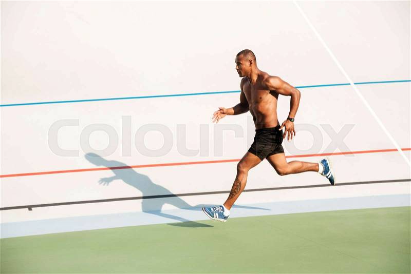 Full length portrait of a strong half naked sportsman running on a track field outdoors, stock photo