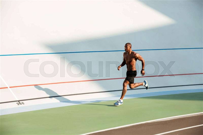 Full length portrait of a muscular half naked sportsman running on a track field outdoors, stock photo