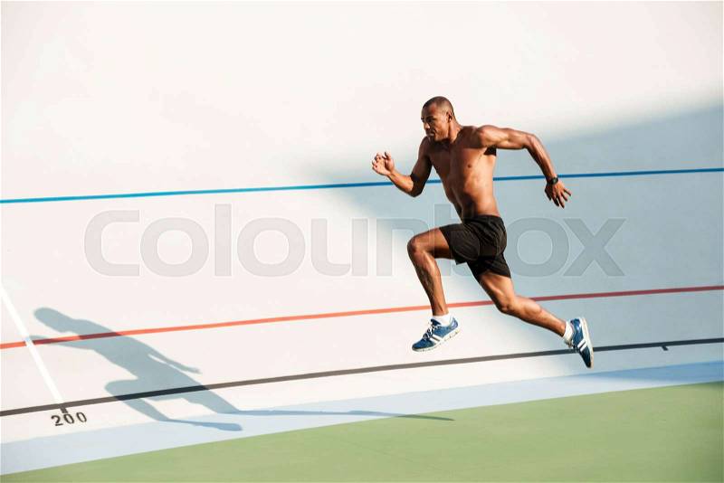 Full length portrait of a athletic half naked sportsman jumping on a track field outdoors, stock photo