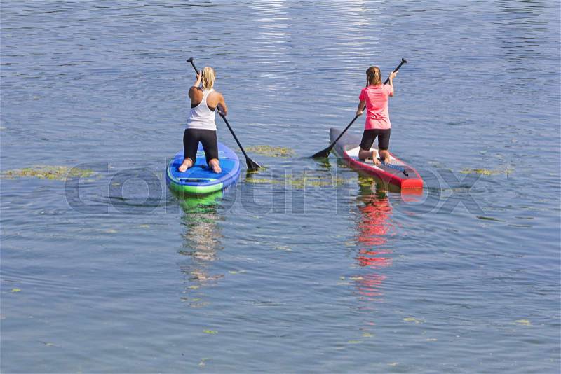 Two women practicing paddle surf in lake, stock photo