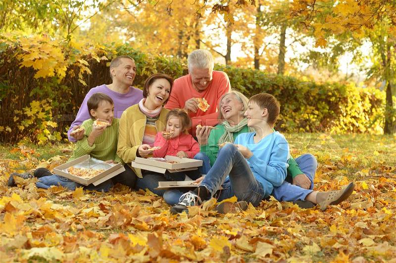 Happy family eating pizza together in autumn park, stock photo