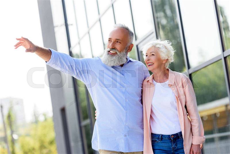 Portrait of senior man showing something to wife while standing on street together, stock photo