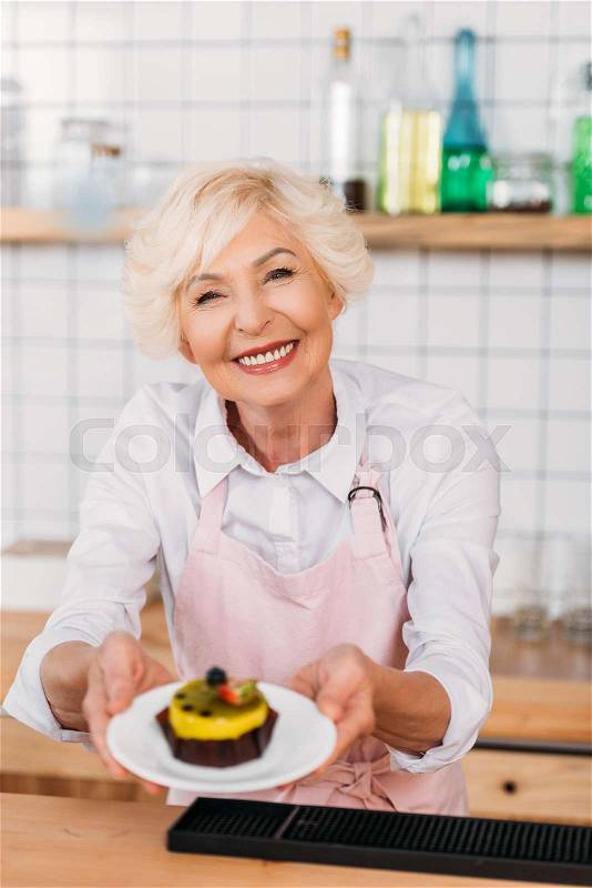 Portrait of smiling coffee shop worker in apron holding plate with dessert in hands, stock photo