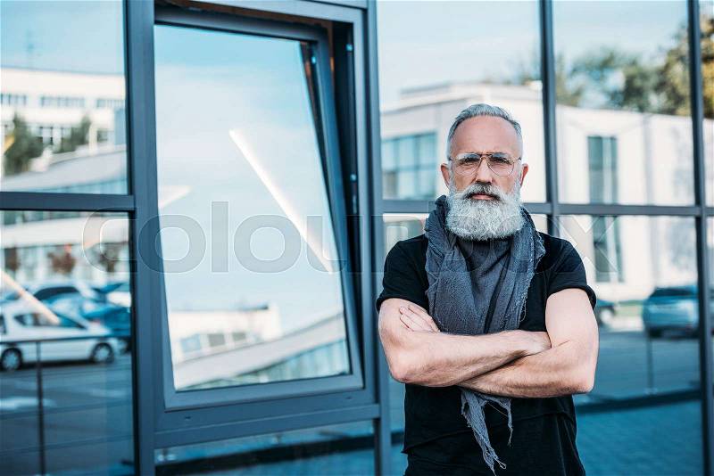 Portrait of senior man with arms crossed looking at camera on street, stock photo