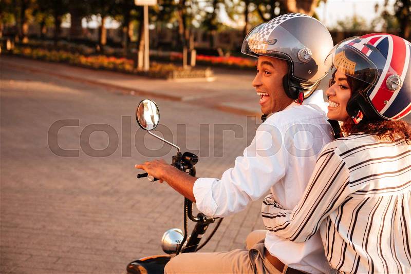 Side view of joyful african couple rides on modern motorbike in park, stock photo