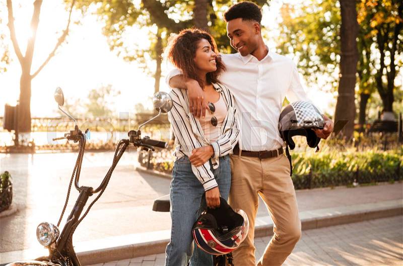 Smiling ee african couple hugging near the modern motorbike in park, stock photo