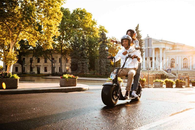 Full length picture of joyful african couple rides on modern motorbike on the street, stock photo