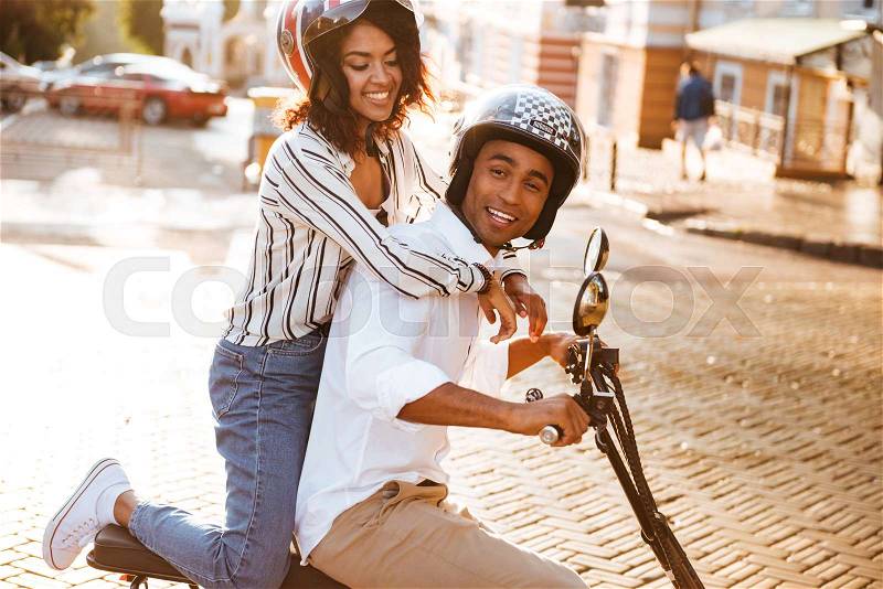Side view of pleased african couple rides on modern motorbike on the street, stock photo