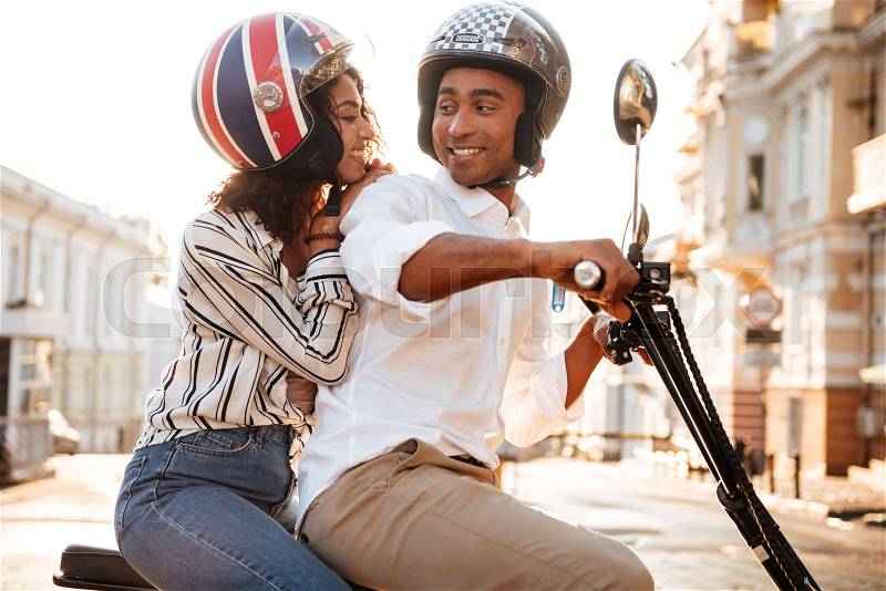 Side view of happy african couple rides on modern motorbike on the street, stock photo