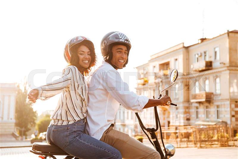 Side view of Carefree young african couple rides on modern motorbike on the street, stock photo