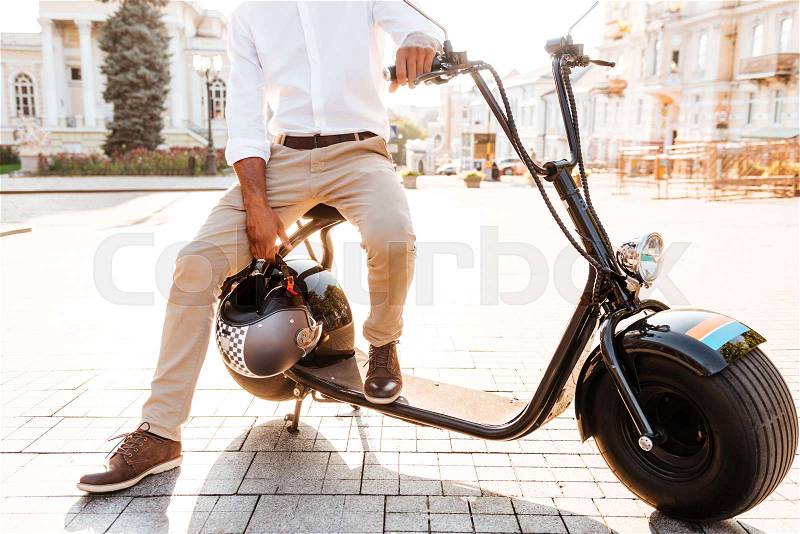 Cropped image of young african man sitting on modern motorbike outdoors, stock photo