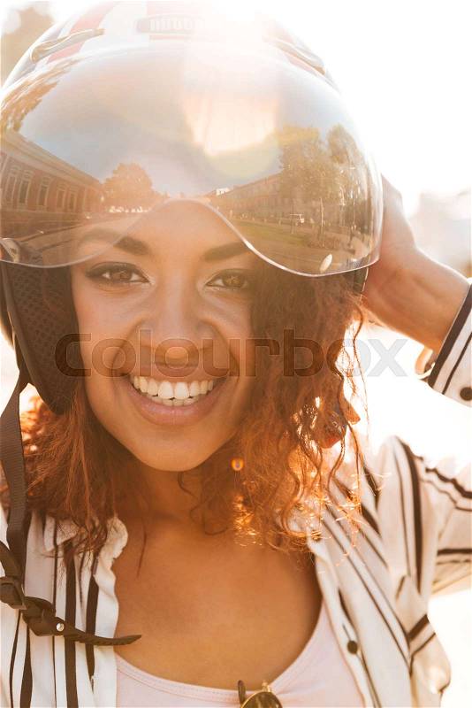 Vertical close up image of happy african woman in moto halmet outdoors and looking at the camera, stock photo