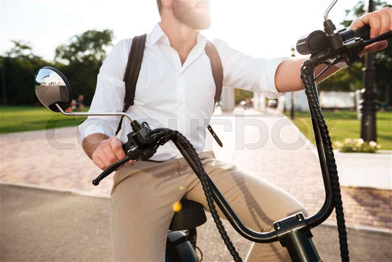Cropped image of bearded man sitting on modern motorbike outdoors, stock photo
