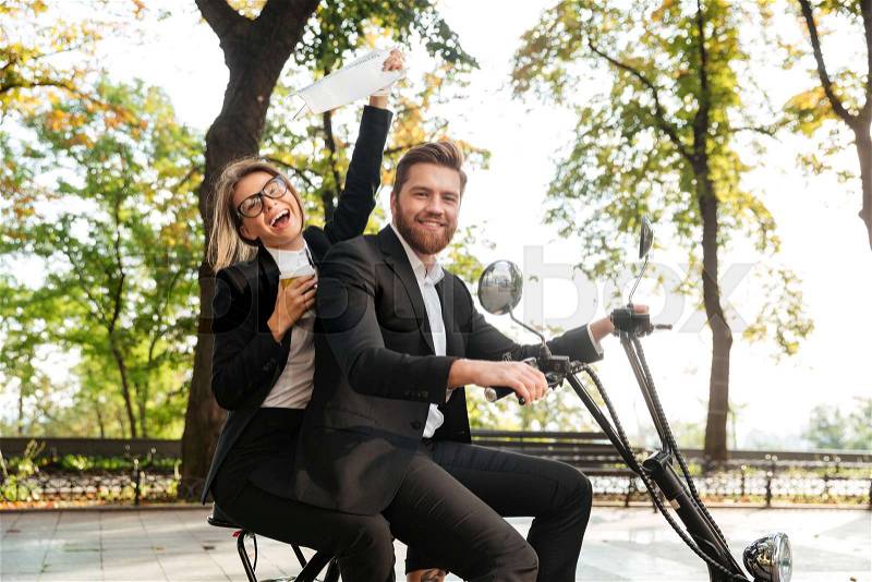 Side view of laughing elegant couple rides on modern motorbike outdoors and looking at the camera, stock photo